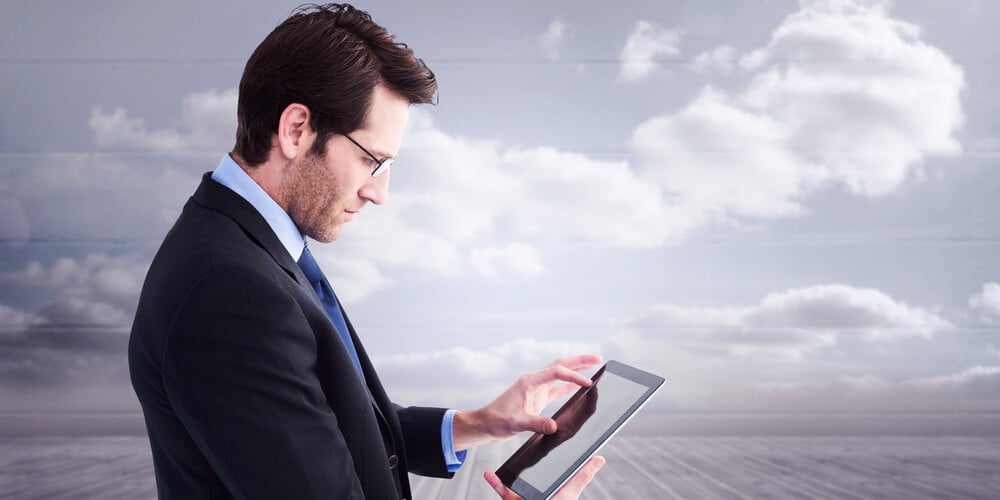 Businessman standing while using a tablet pc against clouds in a room