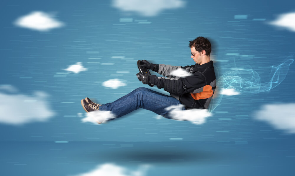 Funny racedriver young man driving between clouds concept on blue background