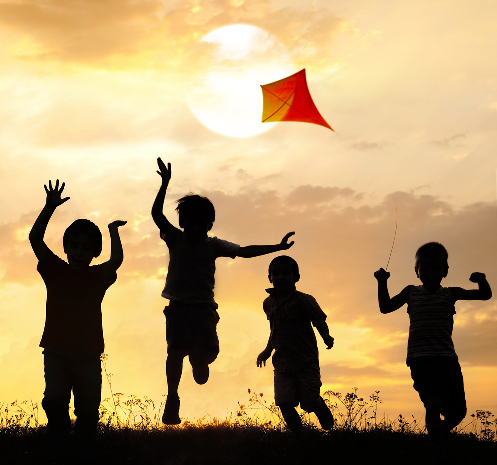 Kids running on summer sunset meadow with kite in fresh hot air