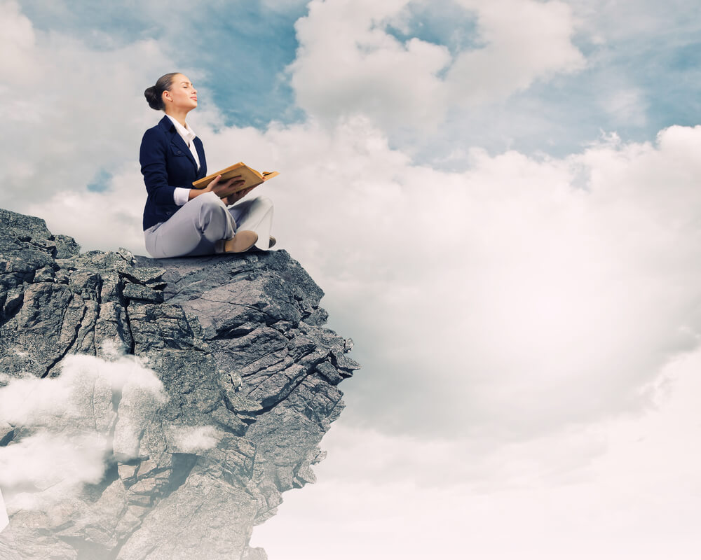 Young attractive businesswoman sitting on top of rock and reading